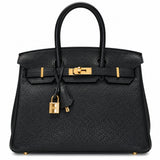 A black pebbled leather handbag with gold-tone hardware, featuring dual top handles, a front strap closure, and a hanging padlock clochette, photographed against a plain white background.