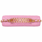 A pink quilted leather shoulder bag with a gold-tone chain strap and a central gold-tone metal bar spelling 'CHANEL' in large letters.