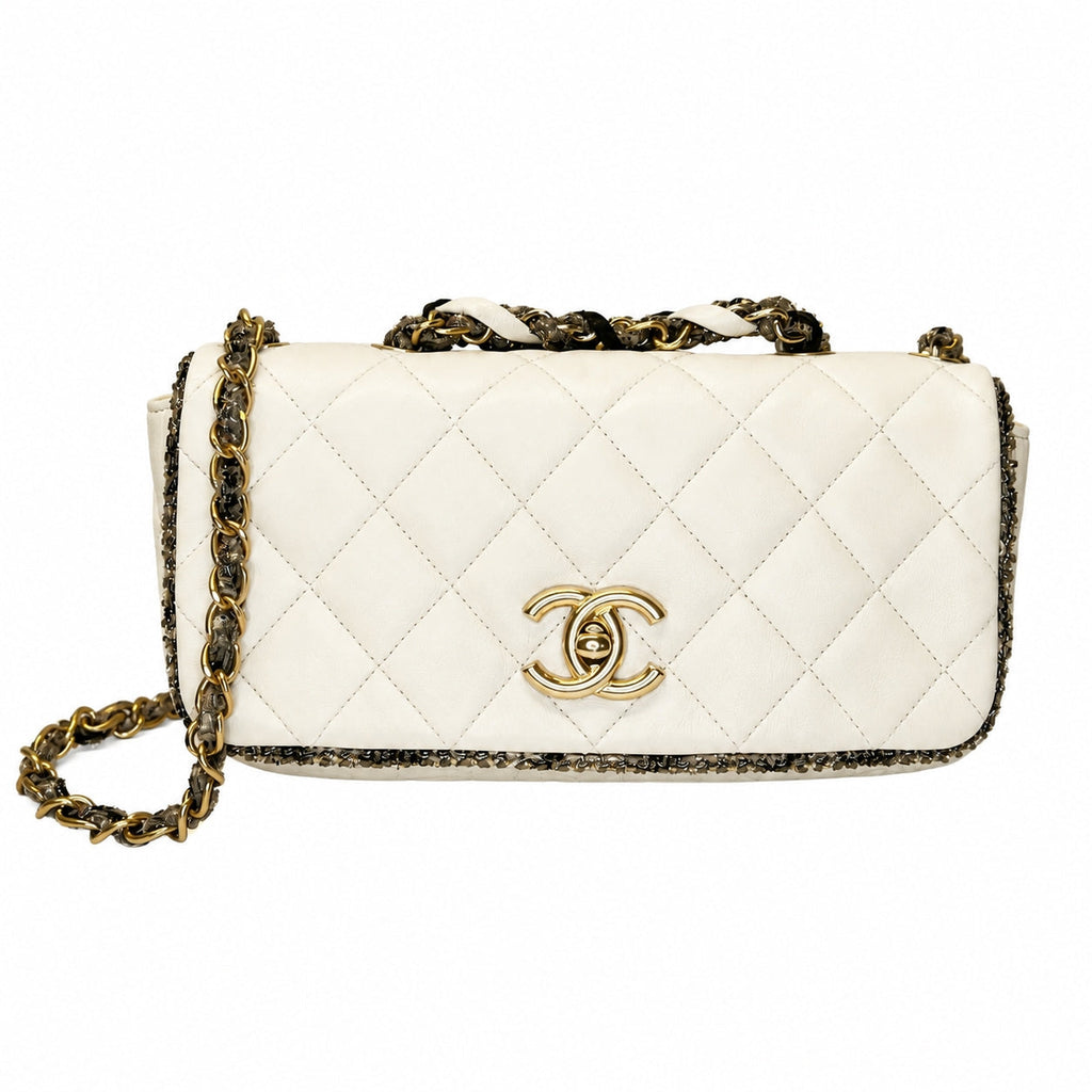 A Chanel shoulder bag in off-white quilted leather with a gold-tone interlocking CC logo, a gold and black chain strap, and a black-and-gold patterned trim, shown against a plain white background.