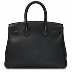 A black pebbled leather handbag with double top handles, structured silhouette, and gold-tone hardware, photographed against a plain white background.