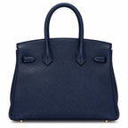 A navy blue pebbled leather handbag with double top handles and gold-tone hardware, photographed against a clean white background.