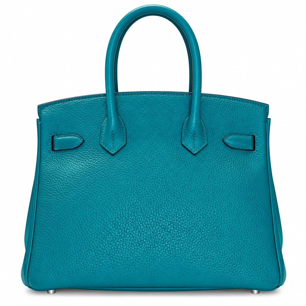 A structured turquoise leather handbag with dual top handles, silver-tone hardware, and small metal feet, photographed against a plain white background.