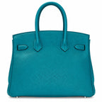 A structured turquoise leather handbag with dual top handles, silver-tone hardware, and small metal feet, photographed against a plain white background.