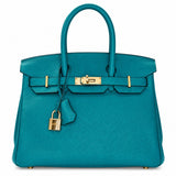 A teal pebbled leather handbag with gold-tone hardware, dual top handles, a front strap closure, and a hanging padlock, photographed on a clean white background.