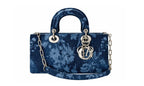 A structured blue velvet handbag with a floral tie-dye pattern, featuring a top handle, silver-tone chain strap, and a hanging interlocking 'D' and 'I' charm on a white background.