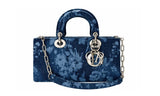 A structured blue velvet handbag with a floral tie-dye pattern, featuring a top handle, silver-tone chain strap, and a hanging interlocking 'D' and 'I' charm on a white background.