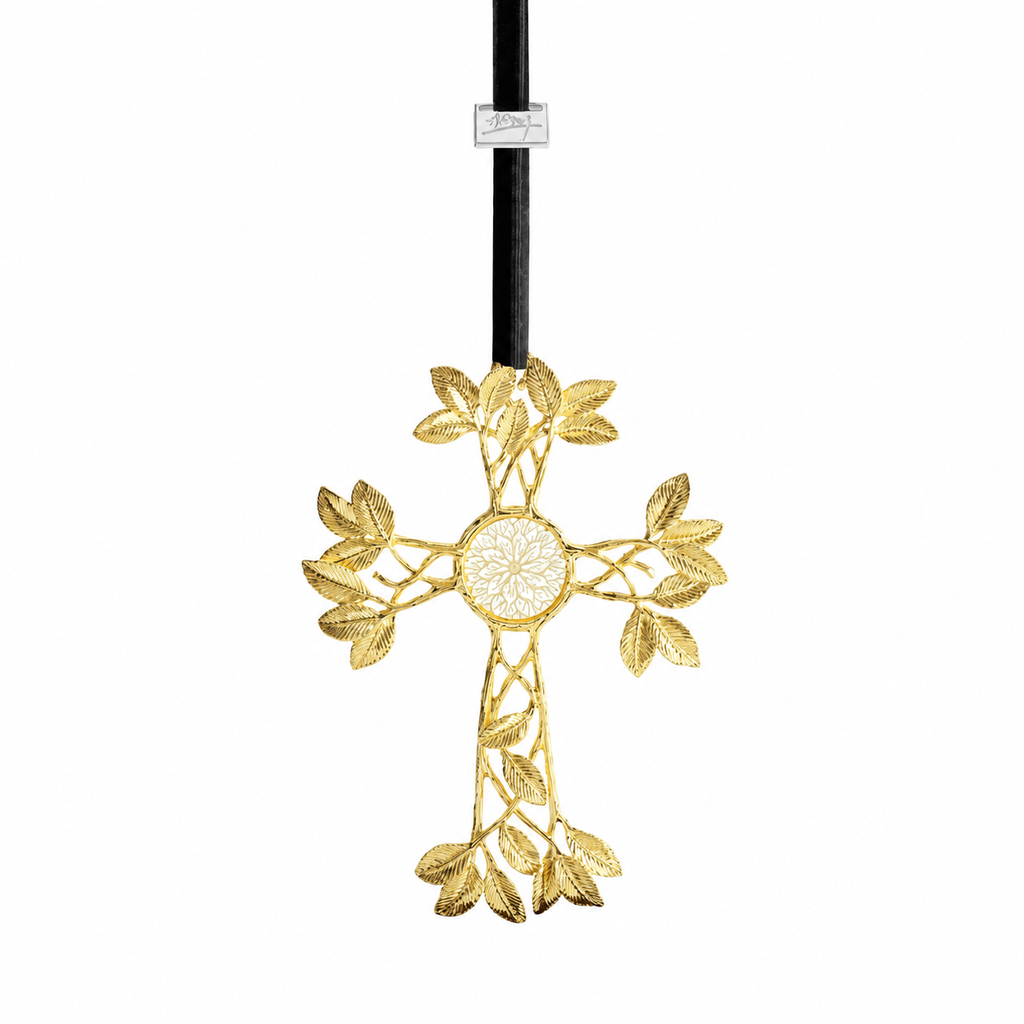 A gold-toned metal cross ornament with leafy vine details and a circular floral center, hanging from a black cord with a small white tag near the top, shown on a plain white background.