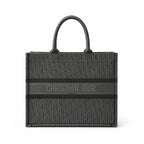 Christian Dior monogram canvas tote bag in dark gray and black, featuring a central horizontal stripe with 'CHRISTIAN DIOR PARIS' text and dual top handles, shown on a plain white background.