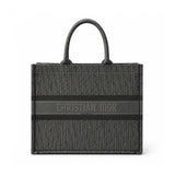 Christian Dior monogram canvas tote bag in dark gray and black, featuring a central horizontal stripe with 'CHRISTIAN DIOR PARIS' text and dual top handles, shown on a plain white background.